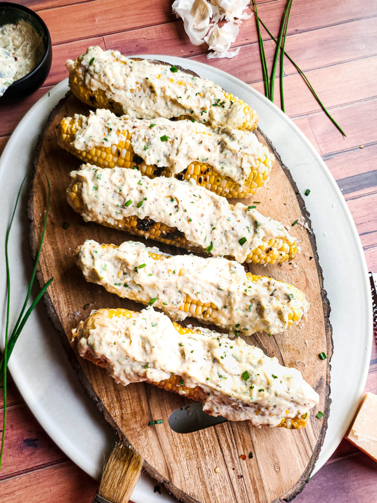 Grilled corn on a wood platter with garlic parmesan sauce