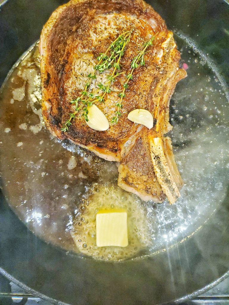 Ribeye steak in a cast iron pan with butter, garlic, and herbs