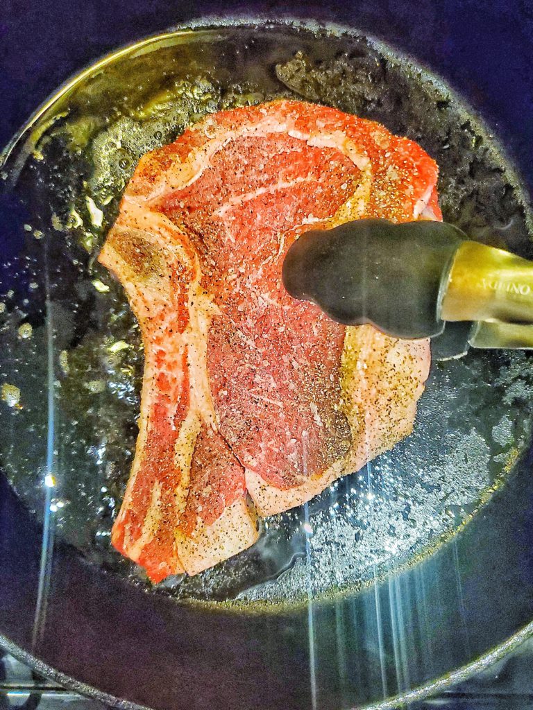 Seasoned rib eye steak in a cast iron pan