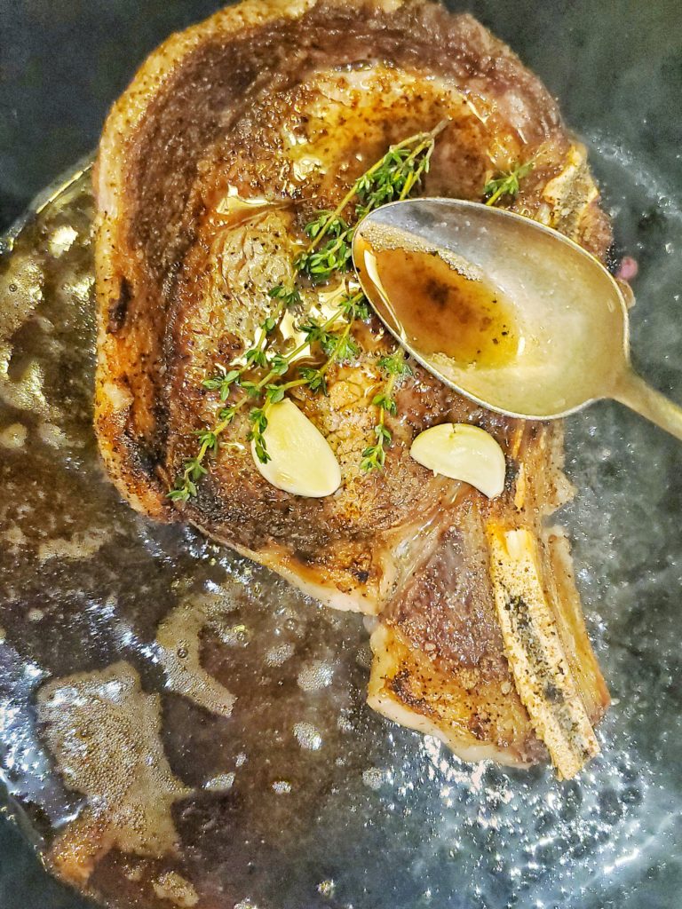Ribeye in a cast iron pan basting with herb garlic butter