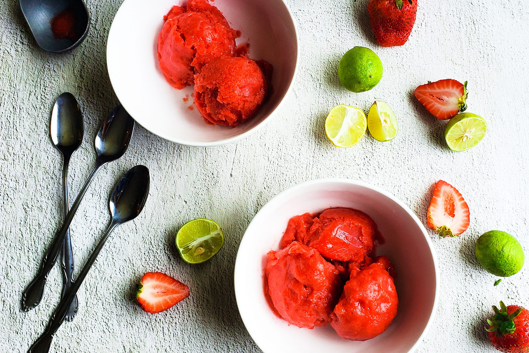 Overhead shot of two bowls of strawberry key lime sorbet in bowls with sliced strawberries and key limes