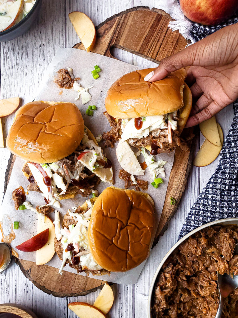 Overhead of Three pulled pork sandwiches topped with slaw on a platter and one sandwich being picked up