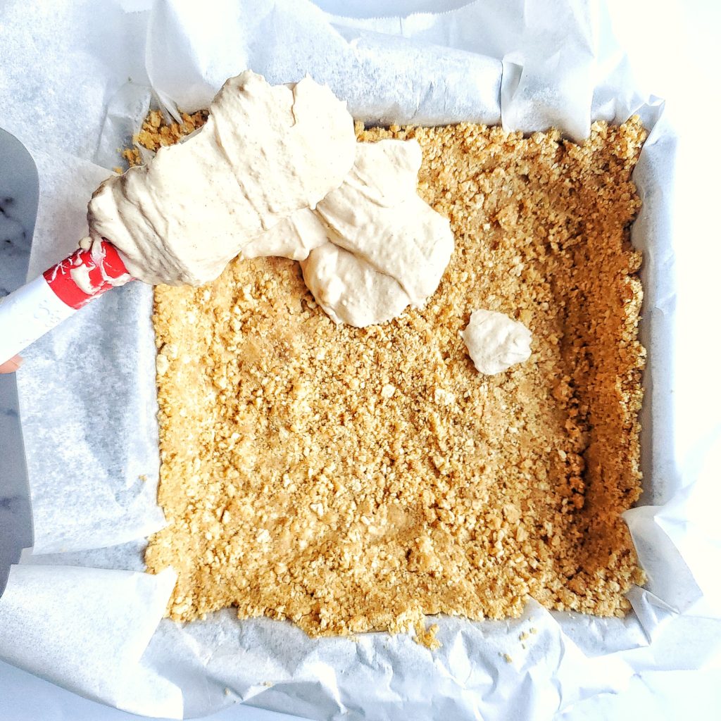 Overhead shot of no bake cheesecake filling being scooped into a graham cracker crust