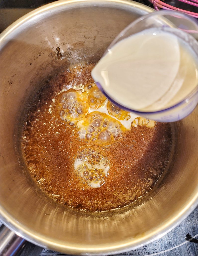Heavy cream poured into a sauce pot of caramel sauce