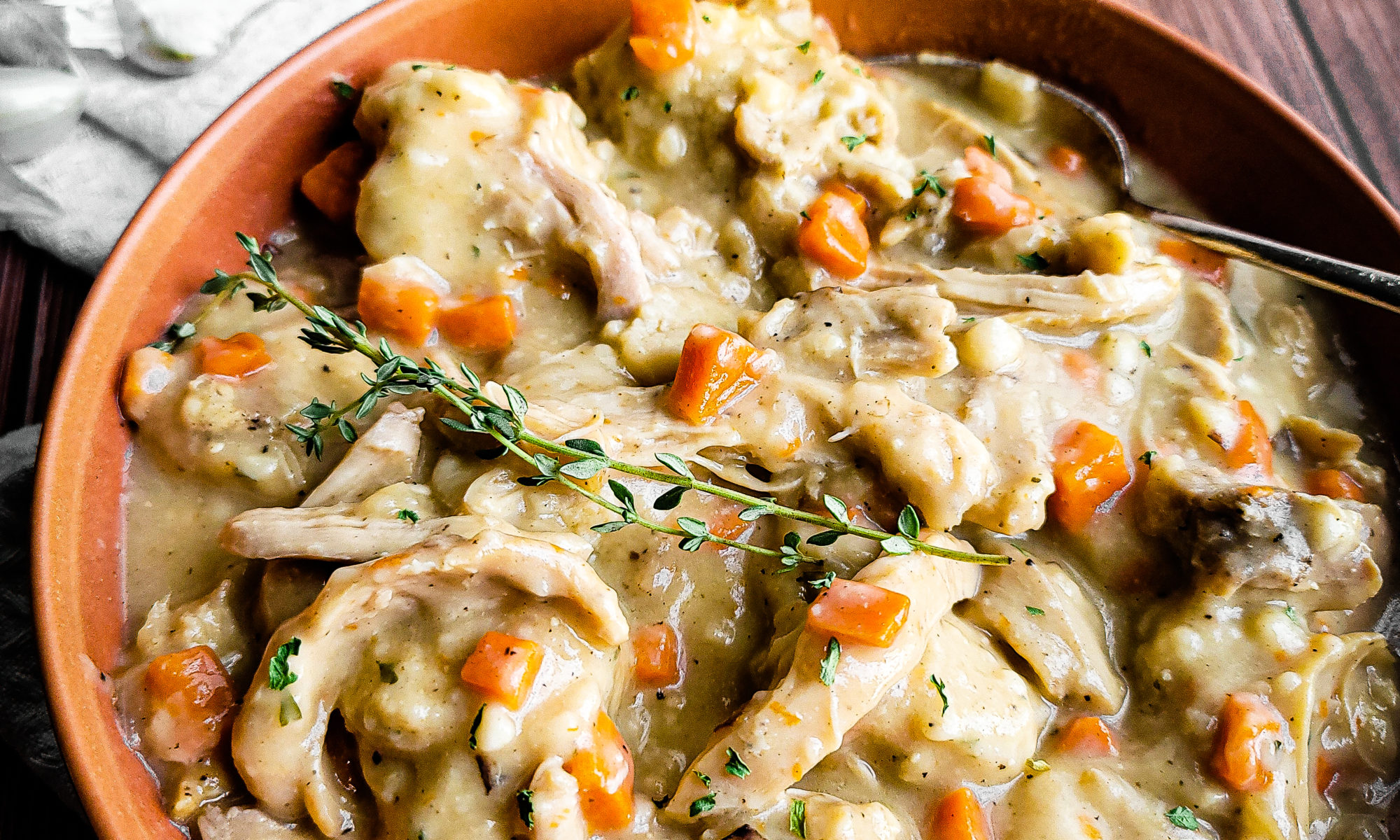 Chicken and dumplings in a bowl with veggies in the background