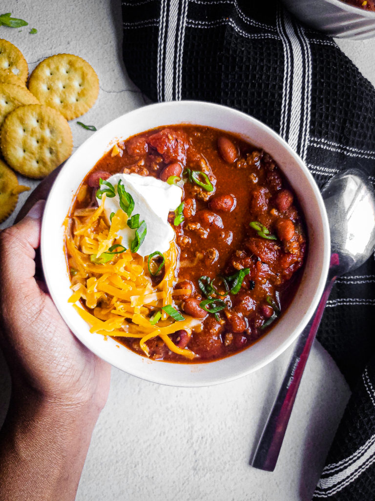 Overhead shot of  a bowl of beef chili with shredded cheese and sour cream