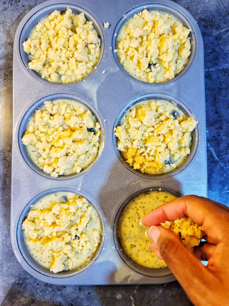 Portioned muffin batter being topped with a streusel crumble